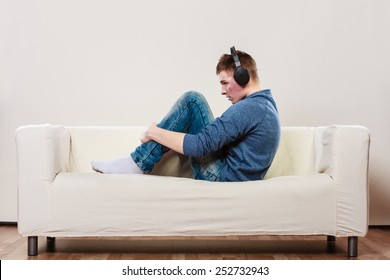 Leisure And Lifestyle Concept. Young Handsome Man With Headphones Sitting On Couch Listening Music At Home, Side View