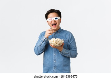 Leisure, Lifestyle And People Concept. Upbeat Smiling Asian Guy In 3d Glasses, Eating Popcorn And Enjoying Interesting Movie, Watching Streaming Service New Tv Series Premier On Awesome TV