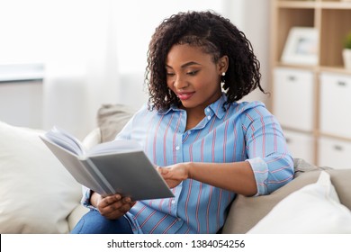 leisure, literature and people concept - smiling african american woman reading book at home