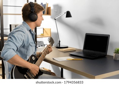 leisure, music and people concept - young man or musician in headphones with laptop computer playing bass guitar sitting at table at home - Powered by Shutterstock