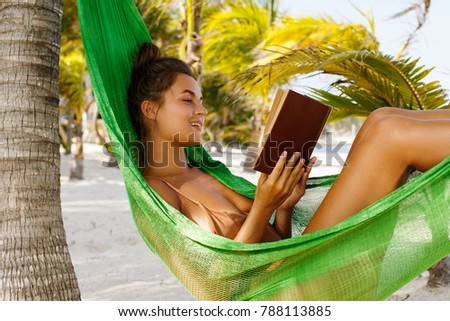 Leisure on the beach. Happy and beautiful woman lying in the hammock, is reading book and enjoy her vacation.