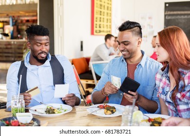 Leisure, Payment And People Concept - Happy Friends With Money And Credit Card Paying Bill For Food At Restaurant