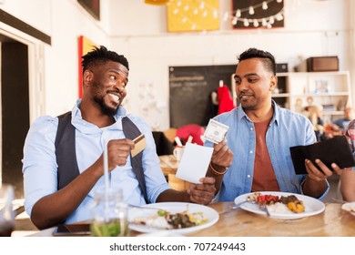 Leisure, Payment And People Concept - Happy Friends With Money And Credit Card Paying Bill For Food At Restaurant