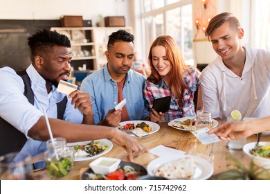 Leisure, Payment And People Concept - Happy Friends With Money And Credit Card Paying Bill For Food At Restaurant