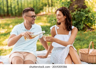 leisure and people concept - happy couple having picnic and pouring wine to glass at summer park