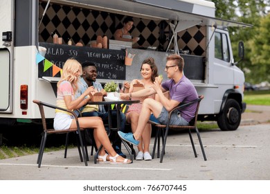 leisure and people concept - happy friends with drinks eating and talking at food truck - Powered by Shutterstock