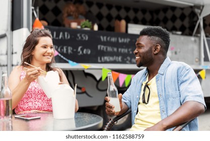 Leisure And People Concept - Happy Mixed Race Couple Eating And Talking At Food Truck