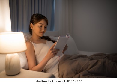 Leisure And People Concept - Young Woman Reading Book In Bed At Night Home