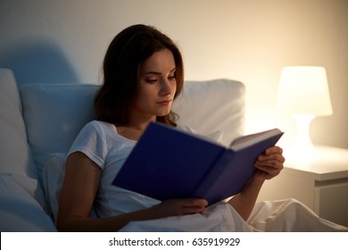 Leisure And People Concept - Young Woman Reading Book In Bed At Night Home