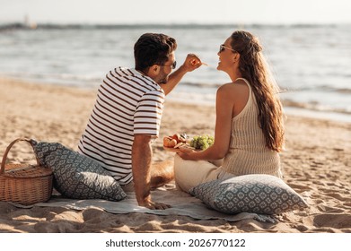 leisure, relationships and people concept - happy couple with food eating and having picnic on beach