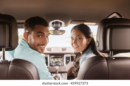 Leisure, Road Trip, Travel And People Concept - Happy Man And Woman Driving In Car And Looking Back