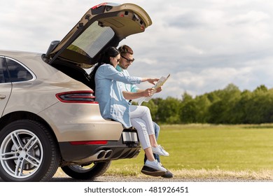 Leisure, Road Trip, Travel And People Concept - Happy Man And Woman Searching Location On Map Sitting On Trunk Of Hatchback Car Outdoors