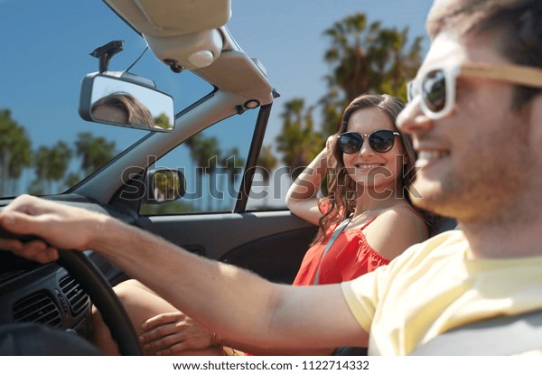 leisure, road trip, travel, summer holidays\
and people concept - happy couple driving in convertible car over\
venice beach background in\
california