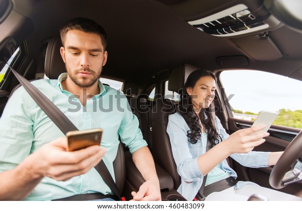 leisure, road trip,\
travel, technology and people concept - happy man and woman with\
smartphones driving in\
car
