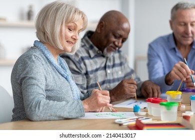 Leisure for senior people at nursing house concept. Good-looking senior woman enjoying painting activity with her multiracial friends, drawing with brush, attending art and craft class - Powered by Shutterstock