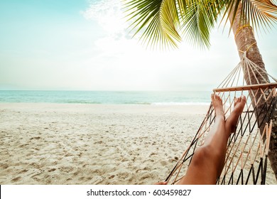 Leisure in summer - Beautiful Tanned legs of sexy women. relax on hammock at sandy tropical beach. vintage color styles