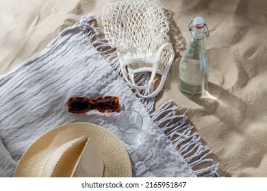 Leisure And Summer Holidays Concept - String Bag, Sunglasses, Glass Bottle Of Water, Straw Hat And Beach Blanket On Sand