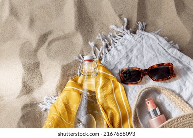 Leisure And Summer Holidays Concept - Sunscreen In Bag, Sunglasses, Bottle Of Water, Pareo And Beach Blanket On Sand