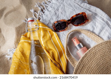 Leisure And Summer Holidays Concept - Sunscreen In Bag, Sunglasses, Bottle Of Water, Pareo And Beach Blanket On Sand