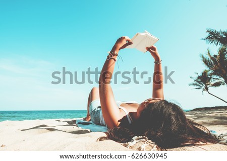 Leisure in summer - Young women lying on a tropical beach, relax with book. Blue sea in the background. Summer vacation concept. vintage color tone.