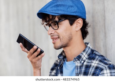 leisure, technology, communication and people concept - smiling hipster man using voice command recorder or calling on smartphone at street wall - Powered by Shutterstock