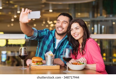 Leisure, Technology, Date, People And Holidays Concept - Happy Couple Having Dinner And Taking Selfie By Smartphone At Restaurant