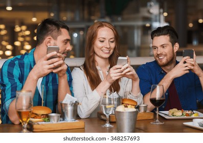 leisure, technology, lifestyle and people concept - happy friends with smartphones dining at restaurant - Powered by Shutterstock