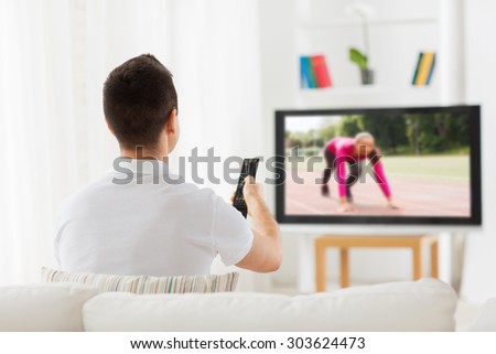 leisure, technology, mass media and people concept - man with remote control watching sport channel on tv at home from back