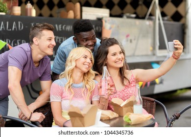 leisure, technology and people concept - happy young friends with food and drinks and taking selfie at food truck - Powered by Shutterstock