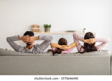 Leisure Time. Back View Of Relaxed Parents And Child With Arms Behind Head Sitting On Couch And Resting At Home, Looking At Empty Wall In Living Room, Copy Space