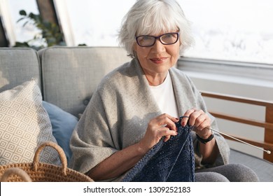 Leisure time, hobby, relaxation, age and handcraft concept. Cheerful charming middle aged woman on retirement relaxing at home, knitting warm sweater for sale, wearing stylish glasses and smiling - Powered by Shutterstock