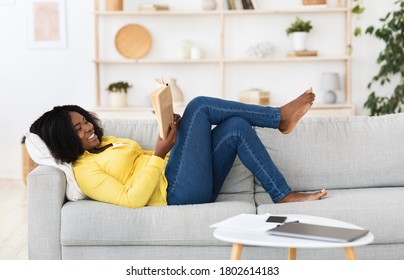 Leisure Time. Smiling Black Woman Reading Paper Book, Lying On Couch At Home, Copy Space