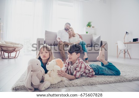 Leisure together. Happy family of four is enjoying at home, small kids are playing with toys, parents are on the sofa, hugging