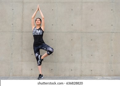 Leisurely Smiling Elegant Female Jogger Showing Yoga Pose Stretching Hands And Feet For Warm Up Motion Before Running Training Standing On Gray Wall Background Outdoor Sidewalk.