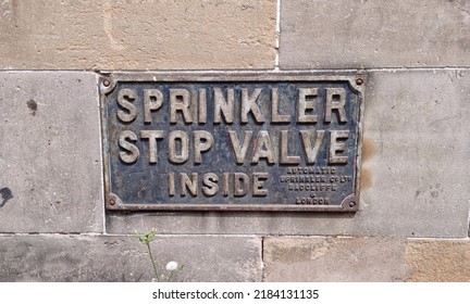 Leith, Edinburgh, Scotland 07 19 2022 Metal Plate Sign Pinned To A Stone Wall Reading  Sprinkler Valve
 Inside In Large Print And  Automatic Sprinkler Co LTD Radcliffe And London In Small Print.