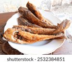 Lele goreng or fried catfish in a white plate on a wooden table. Indonesian traditional food. 