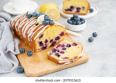 Lemon blueberry cake with lemon icing and fresh berries on top on the board on a gray concrete background with cup of tea. Selective focus. Copy space - Shutterstock ID 2079313615