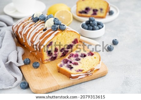 Lemon blueberry cake with lemon icing and fresh berries on top on the board on a gray concrete background with cup of tea. Selective focus. Copy space