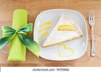 Lemon Cake On A White Porcelain Plate, Dessert Fork And A Napkin Tied With A Bow Green, Wooden Table