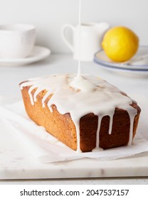Lemon cake with poppy seeds pouring with white icing. Home made sweet morning breakfast on baking paper and marble tray. Cup of tea and fruit on plate on background. Vertical side view - Shutterstock ID 2047537157
