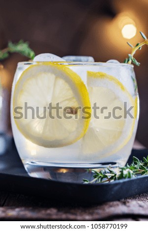 Lemon cocktail with thyme and ice on dark rustic background, close-up. Refreshing alcoholic yellow cocktail drink.