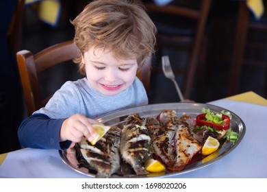 Lemon For Fish. Boy Pours Lemon Juice On Fish In Restaurant. Lunch At The Seaside Cafe. Seafood For Lunch For Children. Delicious Dinner.