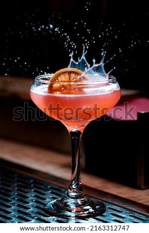 Lemon garnish splashing in pink craft cocktail coupe glass
