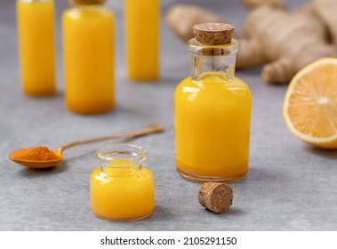 Lemon Ginger Turmeric Shots. Fresh portion of ginger root, lemon juice and turmeric powder drink in a small glass bottles with ingredients on background. Close up, selective focus.
