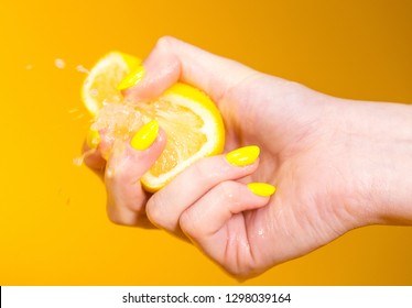 Lemon juice squirts out as hand with yellow fingernails crushes fruit - Shutterstock ID 1298039164