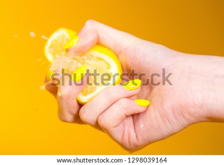 Lemon juice squirts out as hand with yellow fingernails crushes fruit