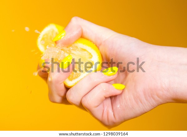 Lemon juice squirts out as hand with yellow\
fingernails crushes fruit