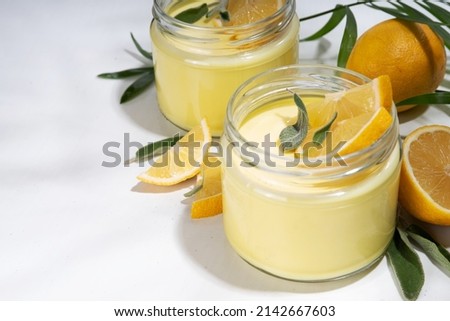 Lemon panna cotta dessert with fresh lemon wedges and sage leaves. Yellow citrus fruit panna cotta in portion jars on a white background