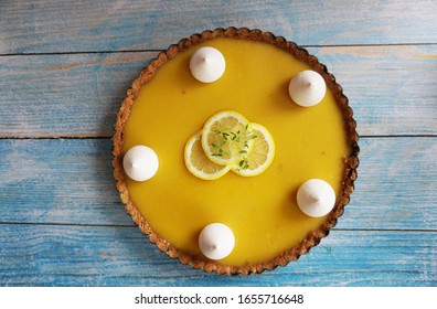 Lemon Pie (tart) With Meringue And Butter Cookie Crust. Blue Wooden Table, Lemon Slices On Top