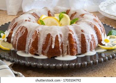Lemon Ricotta Bundt Cake with icing displayed on a black decorative plate with Daisy flowers in a vase in the background.